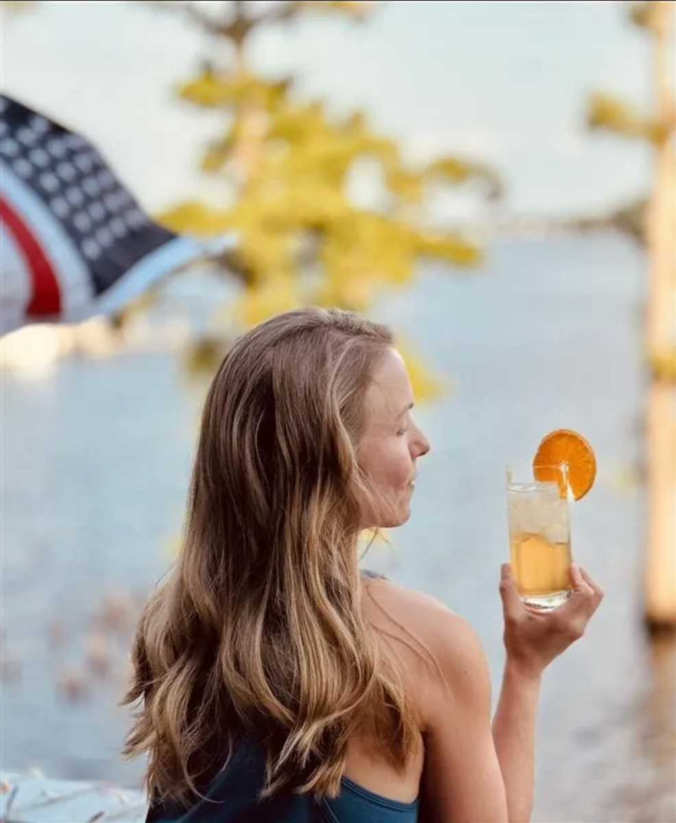 Woman with a drink by the lake, American flag behind her